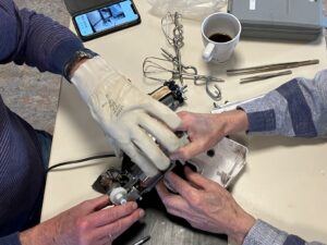 Das Foto zeigt Hände, die gemeinsam ein auf einem Tisch liegendes Elektrogerät reparieren.